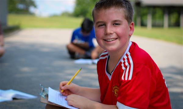 student smiles at camera while writing on clipboard